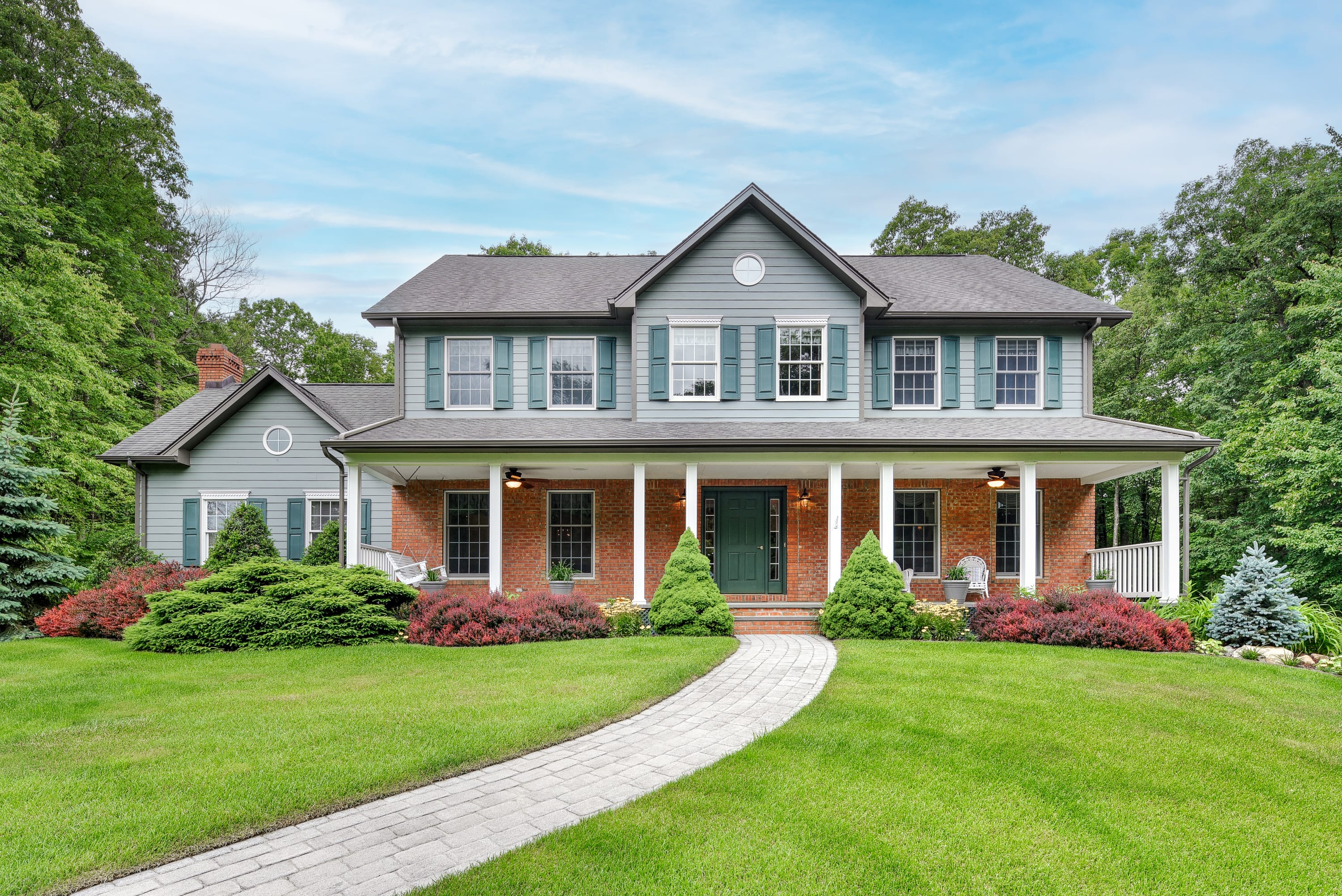 Beautiful two-story colonial home in Kinnelon, Morris County NJ with covered front porch, brick facade, gray siding, and manicured lawn