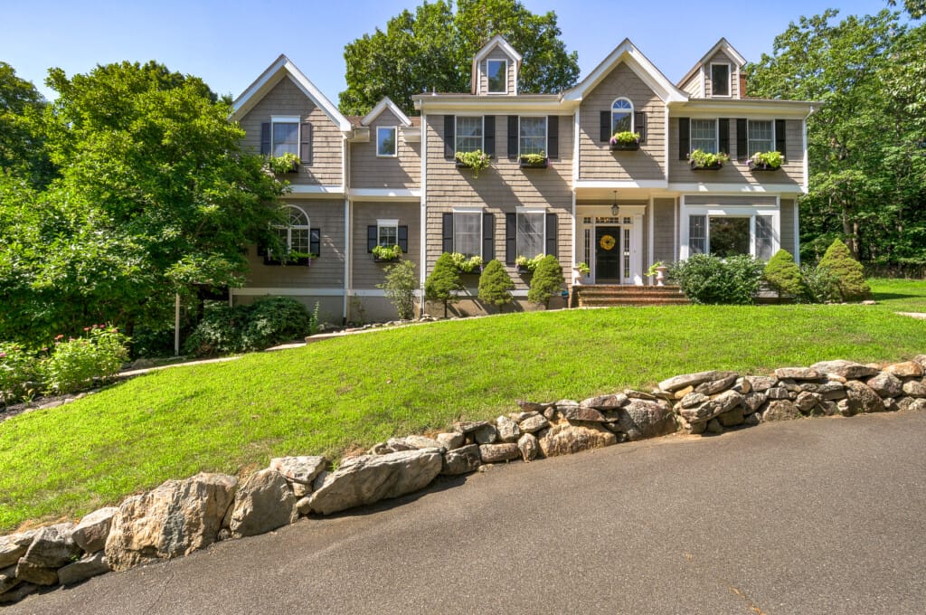 Shingle style home front exterior in Morris County NJ with decorative window boxes, sloped lawn, and stone edging