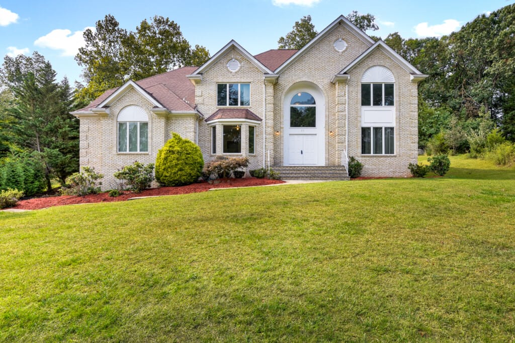 Luxury brick home front elevation in Morris County NJ with arched entry, symmetrical design, and expansive front lawn