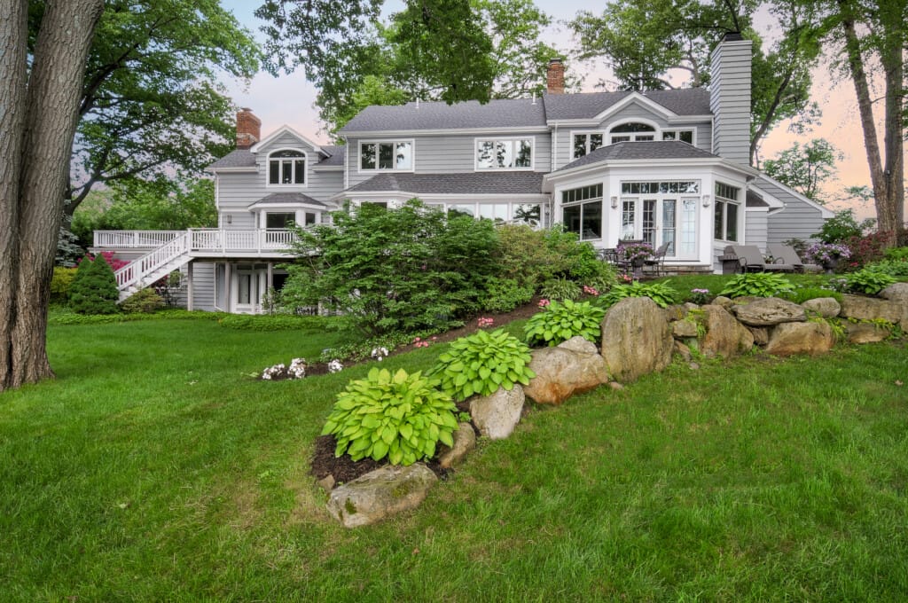 Luxury home rear exterior in Morris County NJ with elevated deck, landscaped yard, and stone garden features