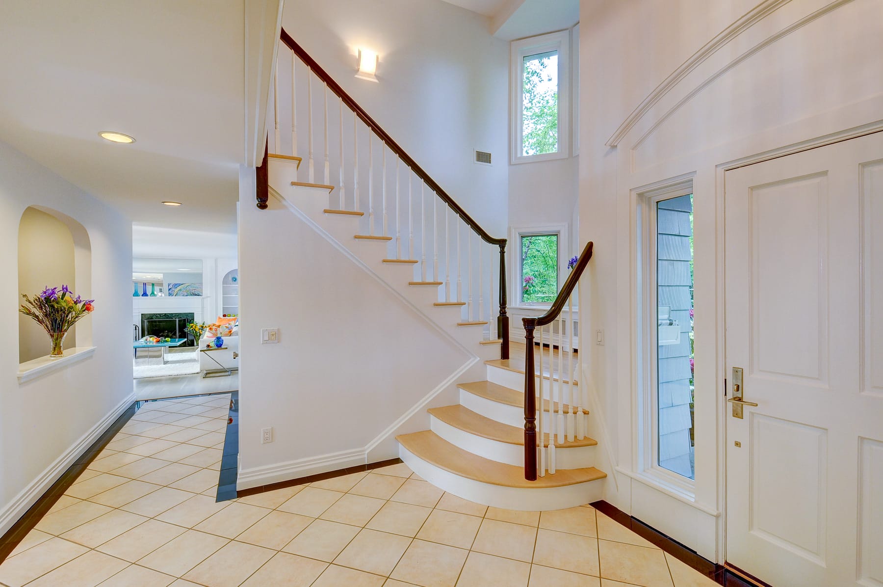 Foyer in Morris County NJ home with curved staircase, tile flooring, and bright natural light leading into living space